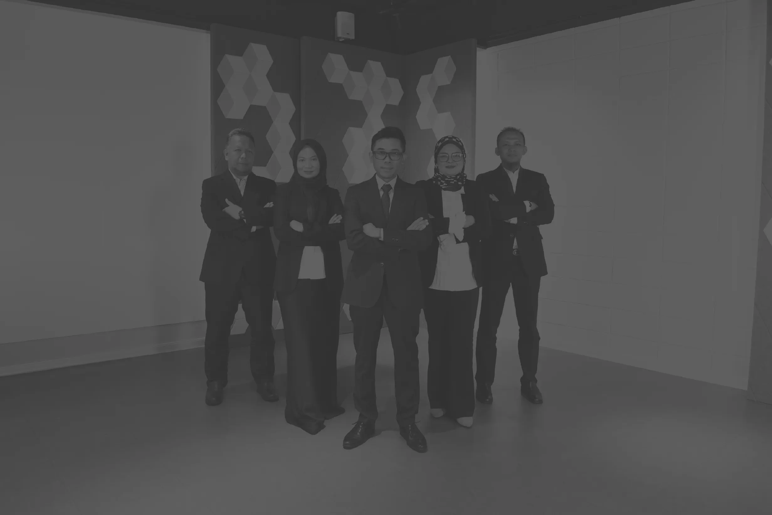 A black and white group photo of five business professionals standing confidently with their arms crossed, posing for a team portrait.